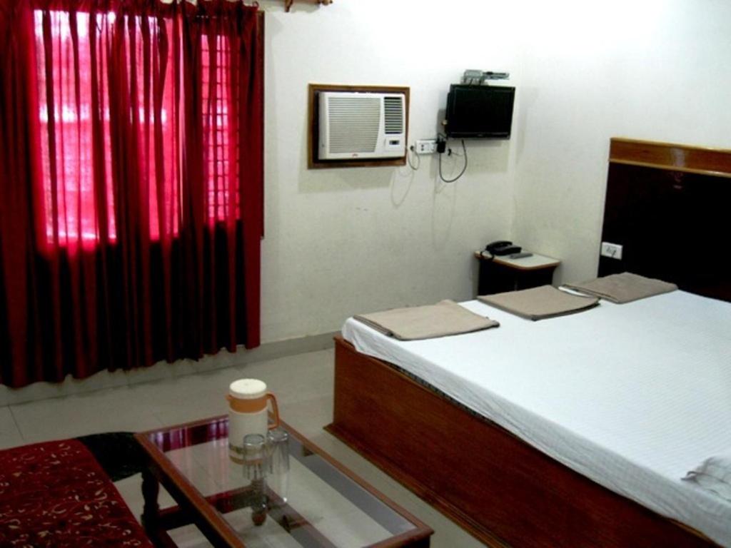 a bedroom with a bed and red curtains and a table at Hotel Ajay International in Agra