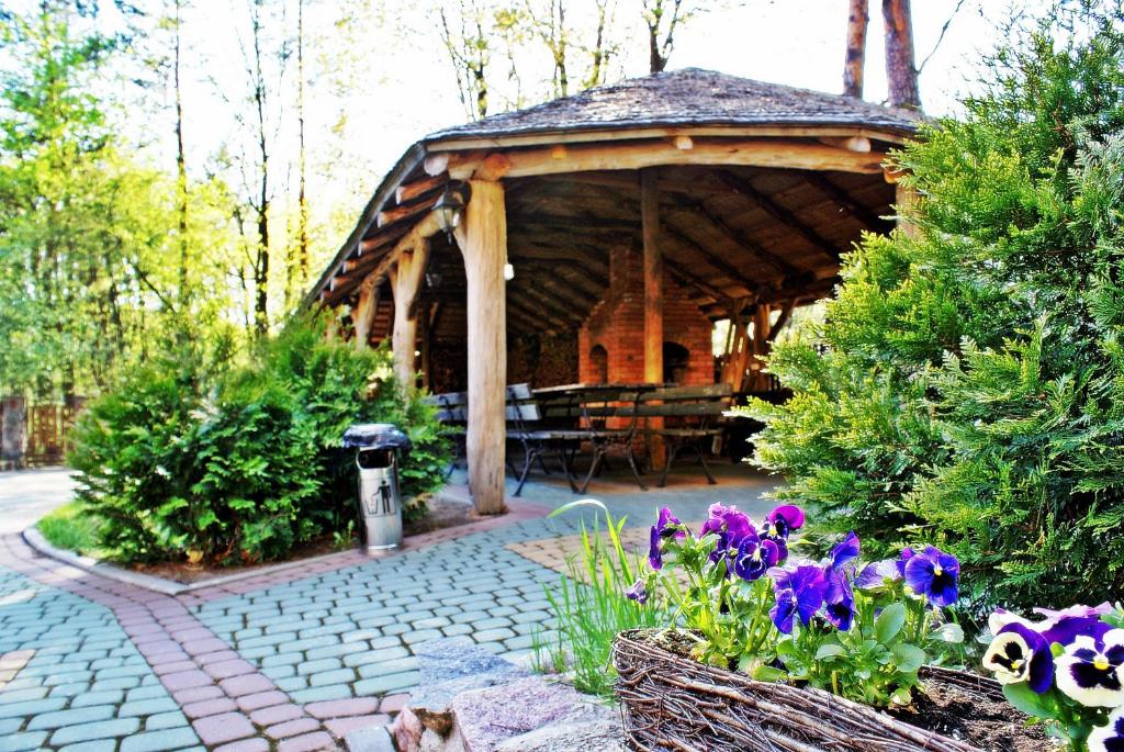 Outdoor seating area under a wooden pavilion, surrounded by greenery and flowers.