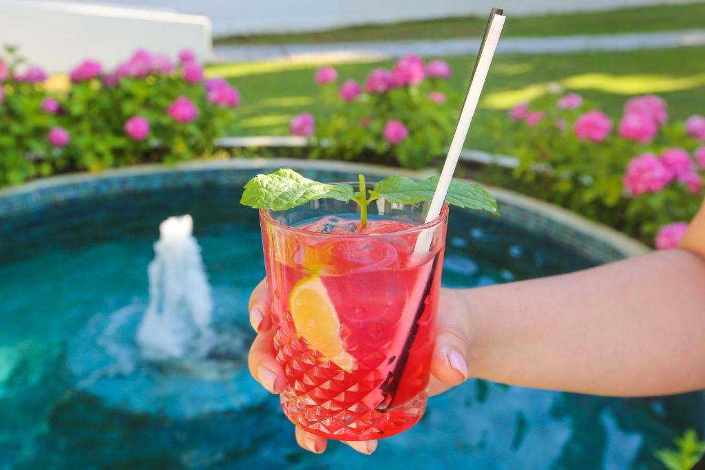 a person holding a drink in their hand next to a pool at Mandraki Village Boutique Hotel in Koukounaries