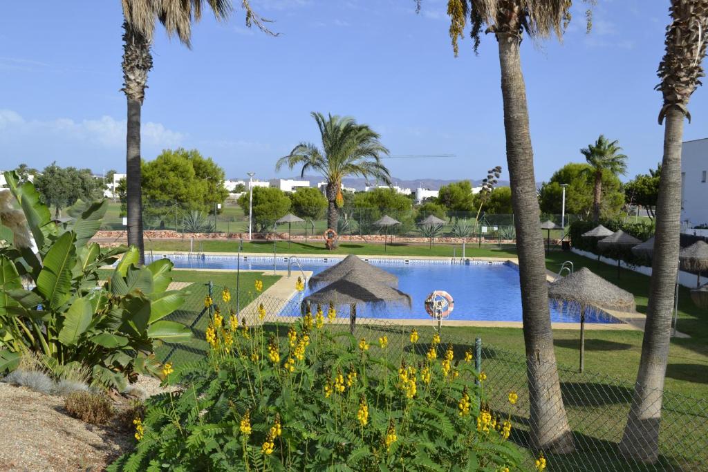 a pool with palm trees and flowers in a park at Apartamento Cabo de Gata in Retamar