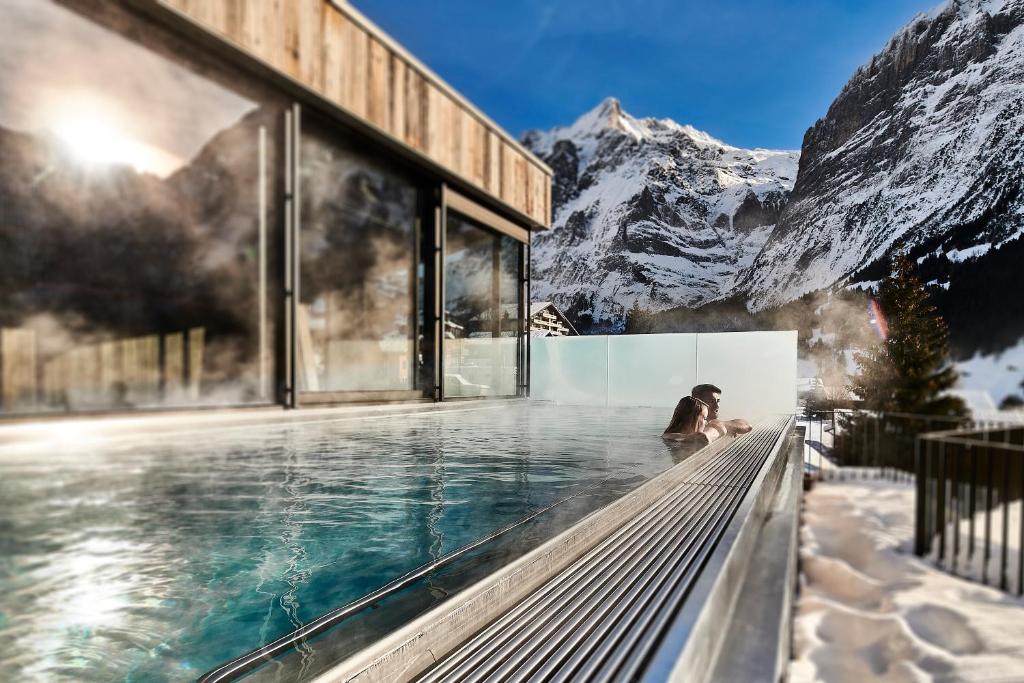 Una donna seduta in una piscina a sfioro con una montagna di Hotel Spinne Grindelwald a Grindelwald