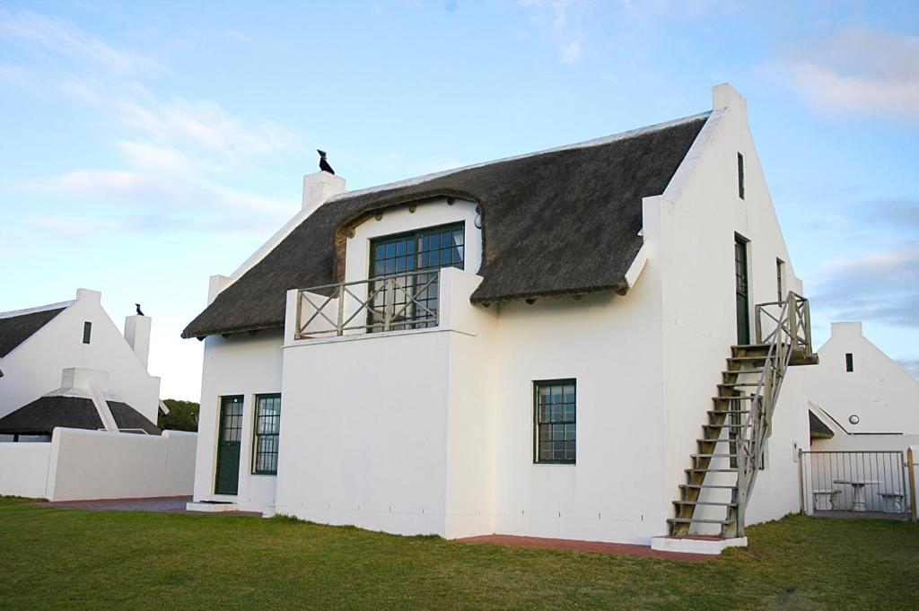 una casa blanca con techo negro en Arniston Seaside Cottages, en Arniston