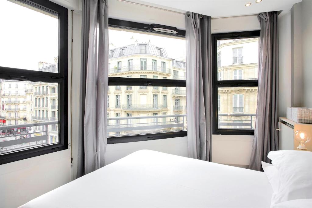 une chambre avec un lit et deux grandes fenêtres dans l'établissement Habitat Parisien - Appartement Opéra Galeries Lafayette, à Paris