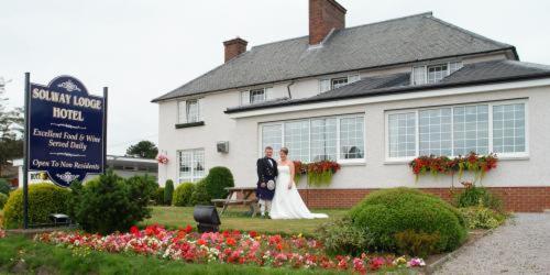 Una novia y un novio parados frente a un edificio en Solway Lodge Hotel, en Gretna Green