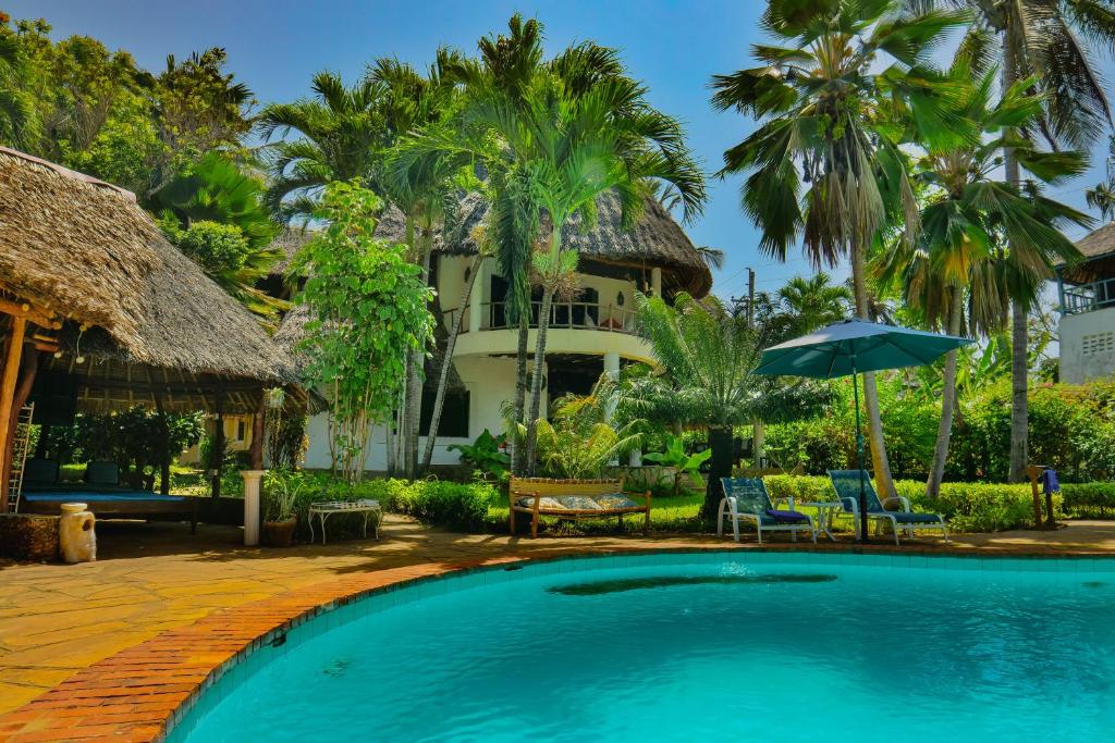 a swimming pool in front of a house with palm trees at Upani in Diani in Diani Beach