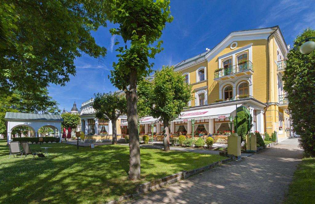 Belvedere Spa & Kurhotel في فرانتيشكوفي لاذنه: مبنى اصفر مع شجرة في حديقة