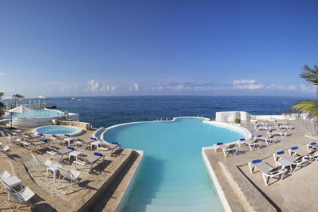 a pool with chairs and the ocean in the background at Private Apartment in Caribe Dominicus 3 SOLO ADULTOS in La Laguna