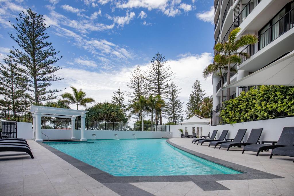 a swimming pool in a building with chairs and trees at Mantra Coolangatta Beach in Gold Coast