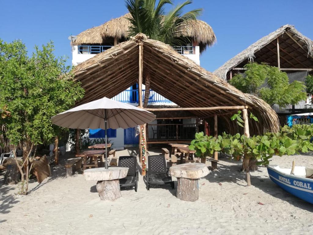 a straw umbrella and tables and chairs on a beach at Hostal Coral Blue in Rincón