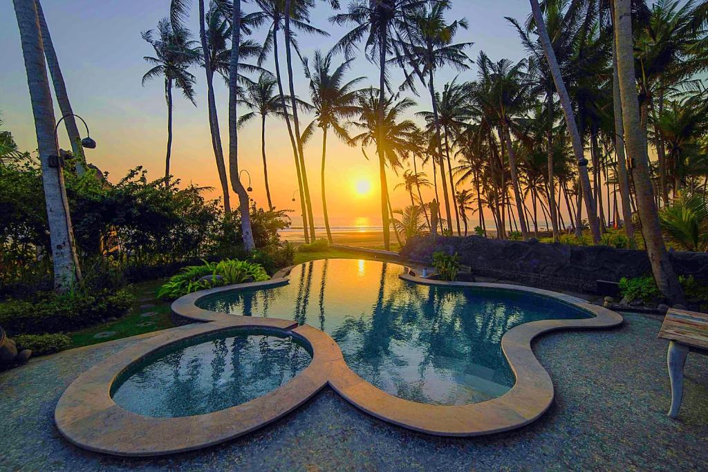 a large swimming pool with a sunset in the background at Tabanan Villas in Tabanan