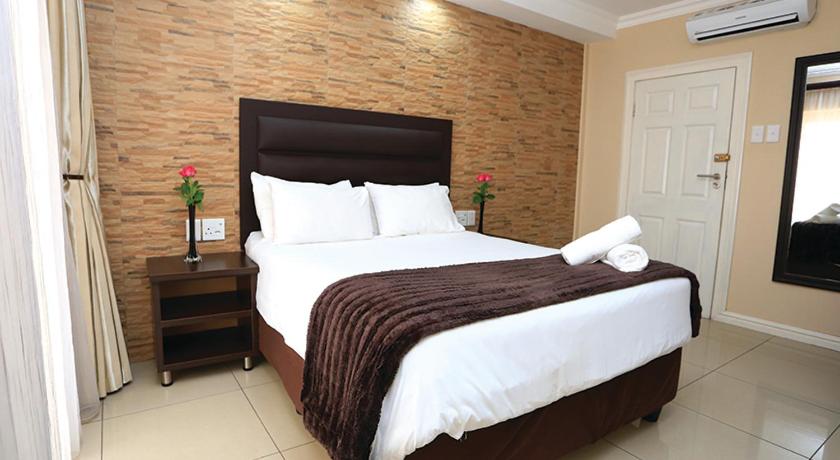a bedroom with a large bed and a brick wall at Bayside Hotel 97 Russell Street in Durban