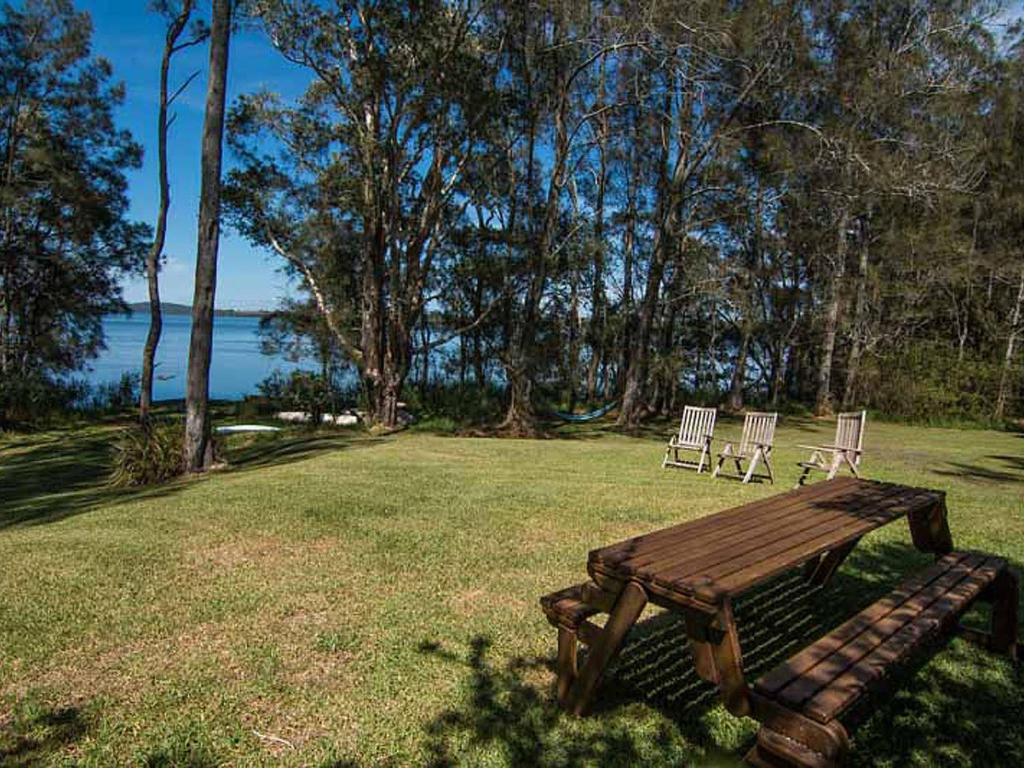 a picnic table and two chairs in a field with the water at Tuppys on the Lake in Neranie