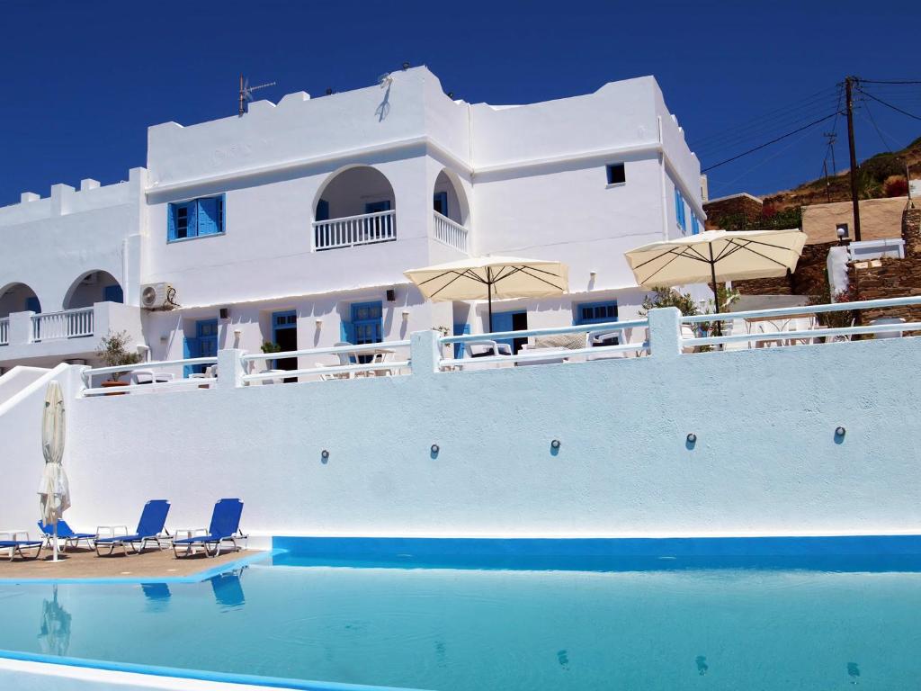 a white building with chairs and umbrellas next to a swimming pool at Hotel Petradi in Ios Chora