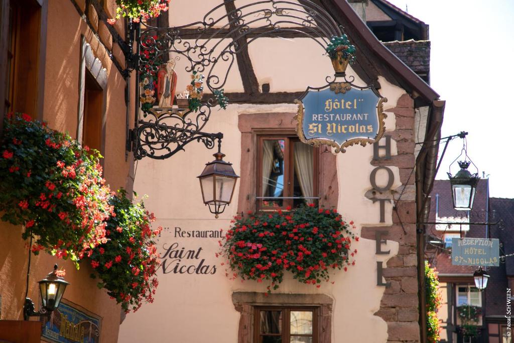 una calle con flores y un cartel en un edificio en Hôtel le Saint Nicolas, en Riquewihr