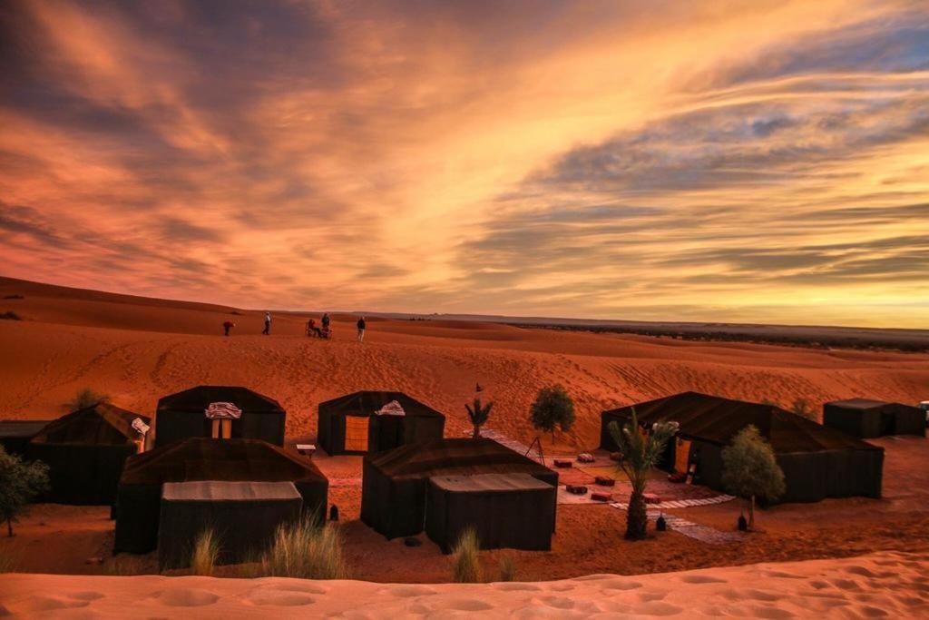 a desert with tents in the sand with a sunset at Camp Sahara Holidays in Mhamid