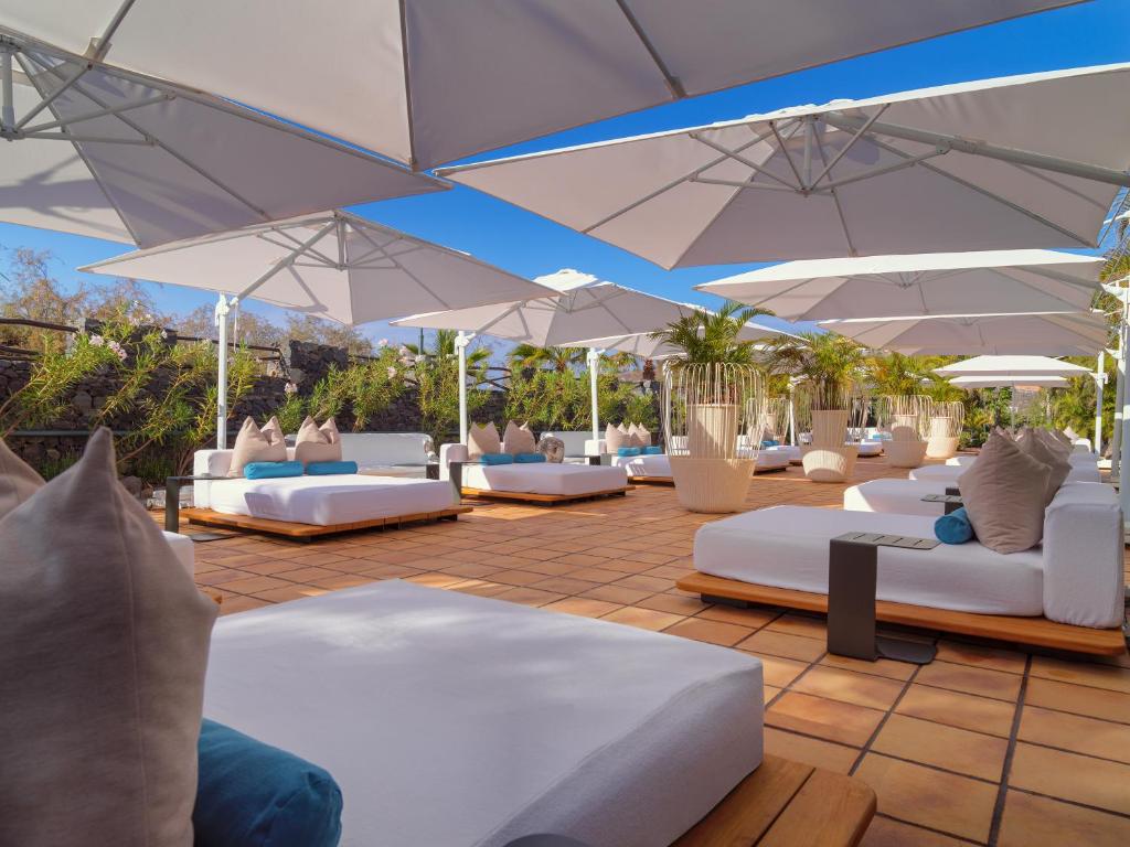 a patio with white couches and umbrellas at Hotel Jardín Tecina in Playa de Santiago