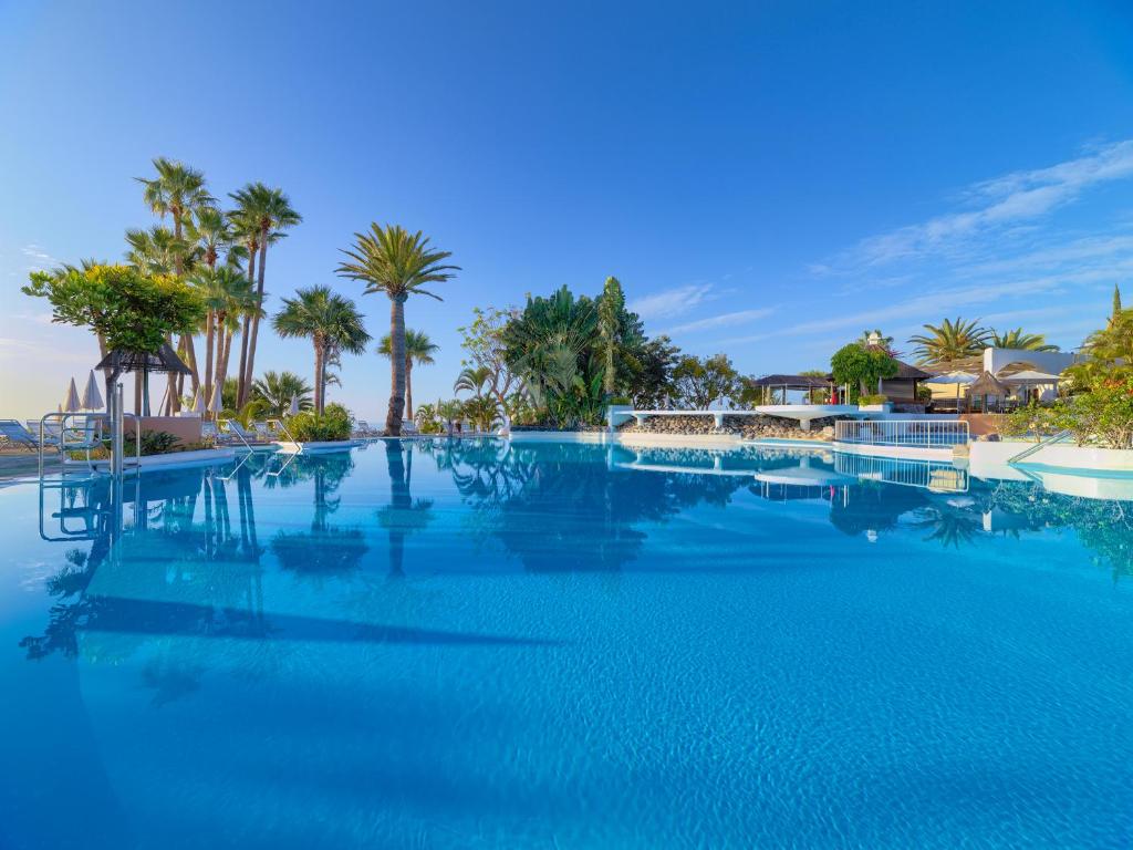 a large swimming pool with blue water and palm trees at Hotel Jardín Tecina in Playa de Santiago