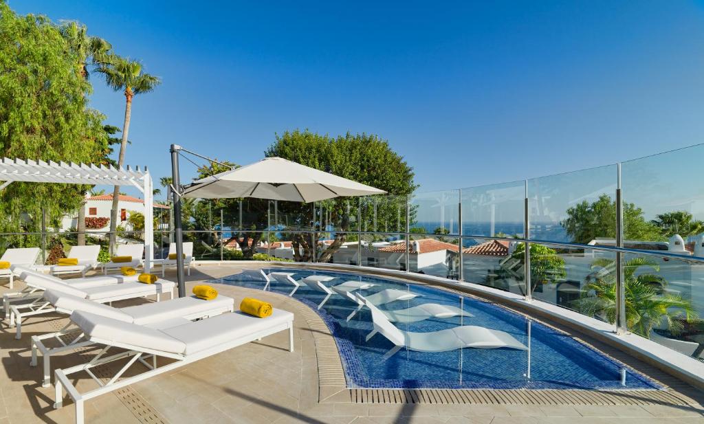 a pool with white lounge chairs and an umbrella at Hotel Jardín Tecina in Playa de Santiago