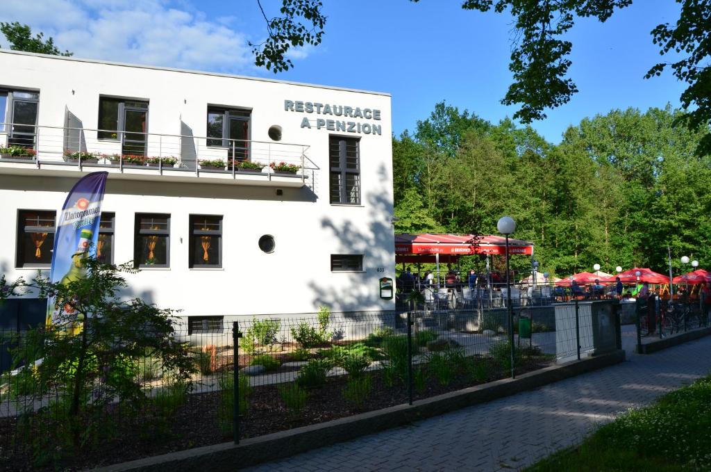 Biały budynek z czerwonymi parasolami przed nim w obiekcie Restaurace a penzion Zděná Bouda w mieście Hradec Králové