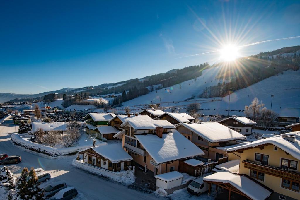 un pueblo cubierto de nieve con el sol en el fondo en Golf & Skipension Krug en Haus im Ennstal