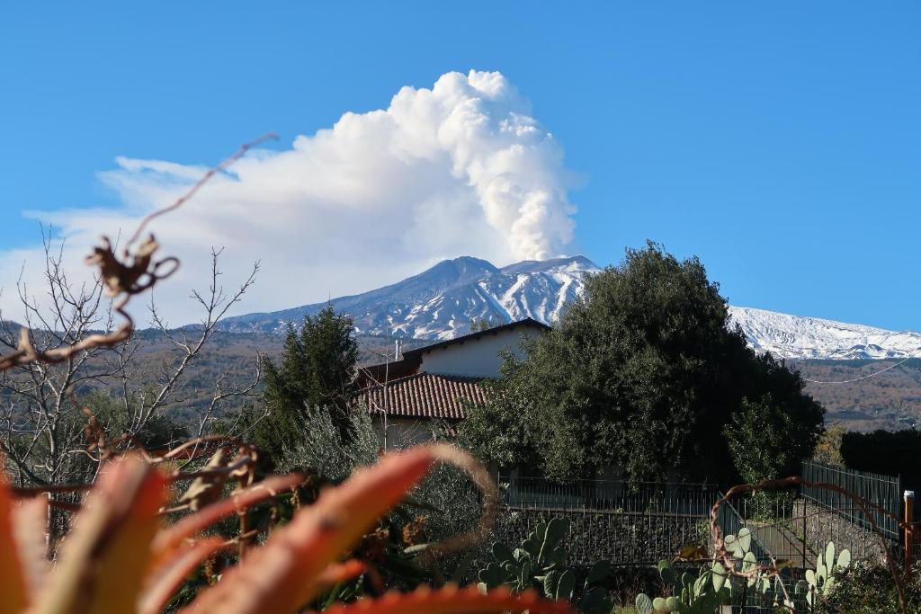 un soffio di fumo che esce da un edificio con una montagna di Agriturismo Etna-Mare a Piedimonte Etneo