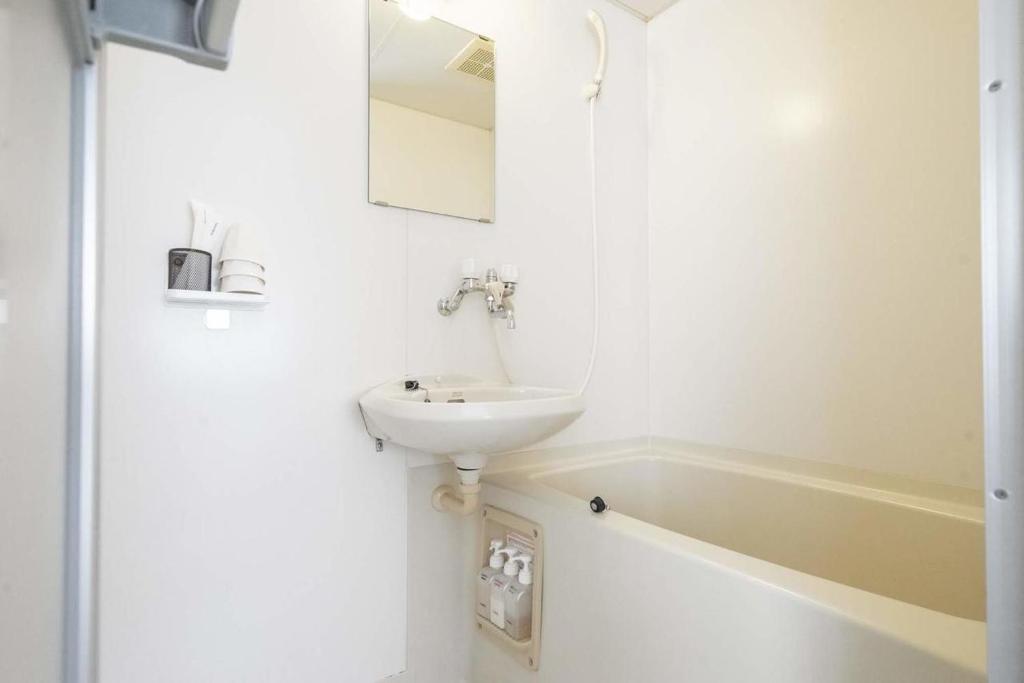 a white bathroom with a sink and a bath tub at Beach Side Inn Shirahama in Shimoda