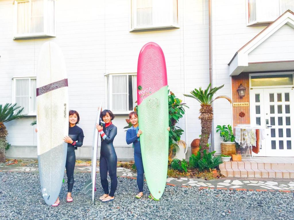 three women are holding surfboards in front of a house at Beach Side Inn Shirahama in Shimoda