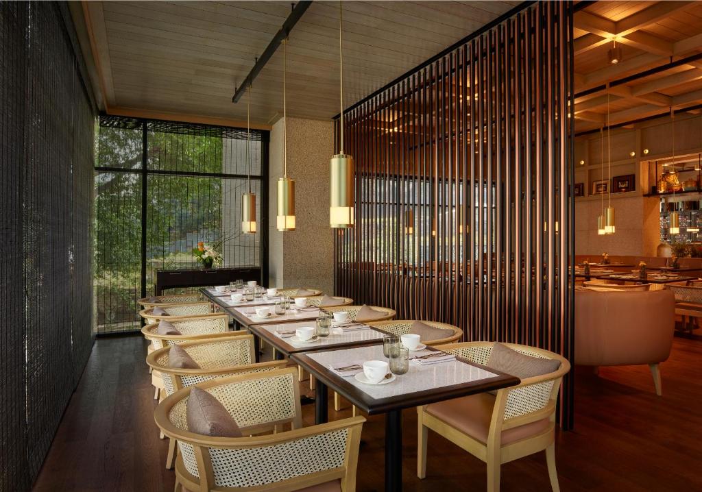 A long breakfast table sits beside tall windows overlooking dense greenery.