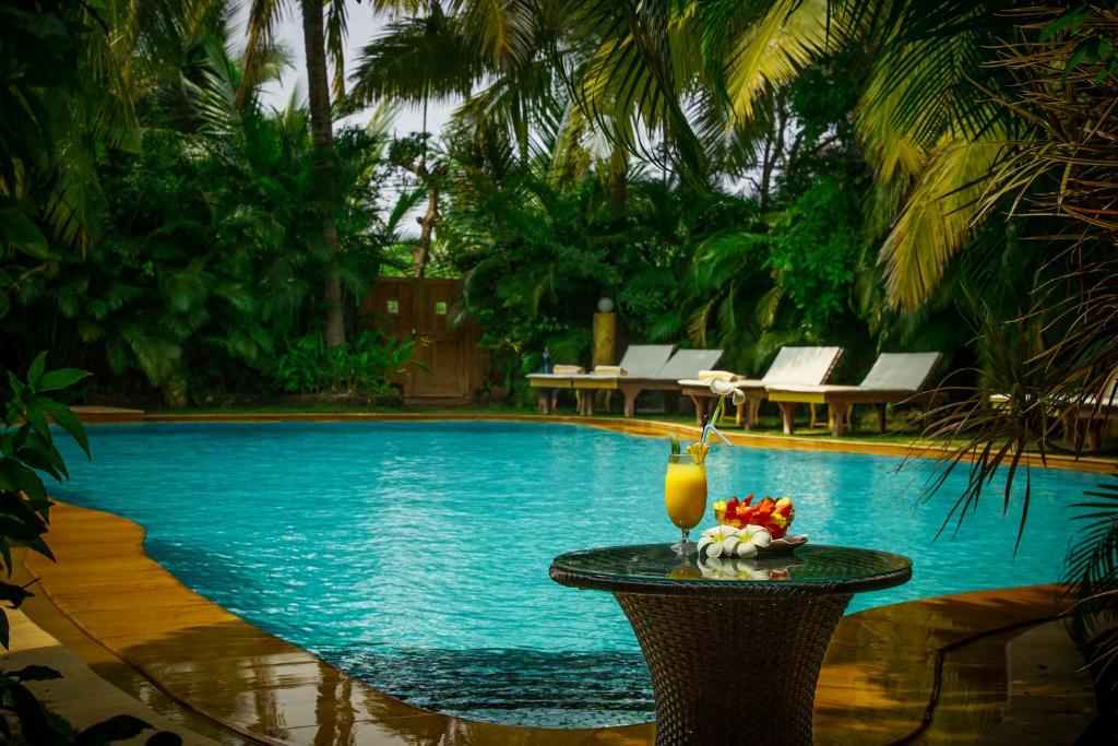 a drink on a table next to a swimming pool at Papa Jolly Eco Resort-Near Morjim Beach in Morjim