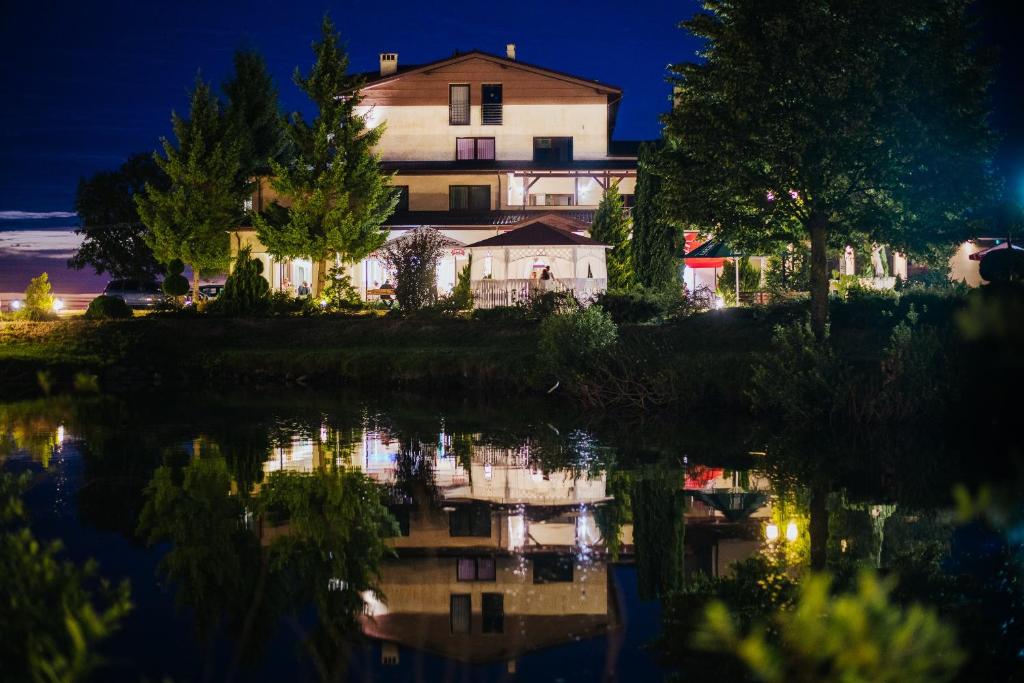 a house sitting next to a lake at night at Hotel Czardasz in Luzino