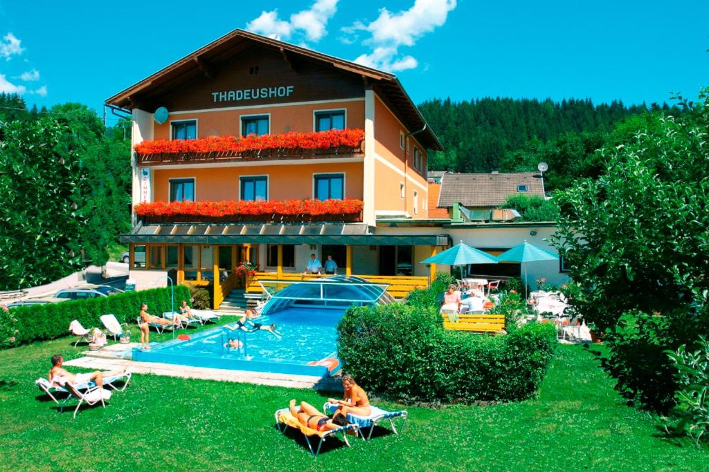 a hotel with a pool and people sitting in the yard at Hotel Restaurant Thadeushof in Techelsberg am Worthersee