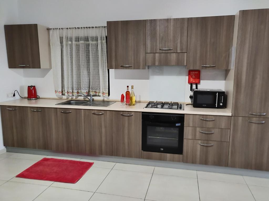 a kitchen with wooden cabinets and a sink and a microwave at Spacious two bedroom apartment within 5 minutes walk from St Thomas Bay in Marsascala in Tas-Santi