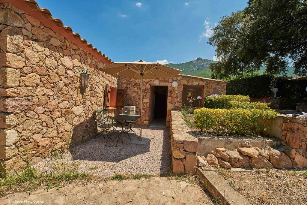 - un bâtiment en pierre avec une table et un parasol dans l'établissement Maison L'Olivier avec piscine, à Cuttoli-Corticchiato