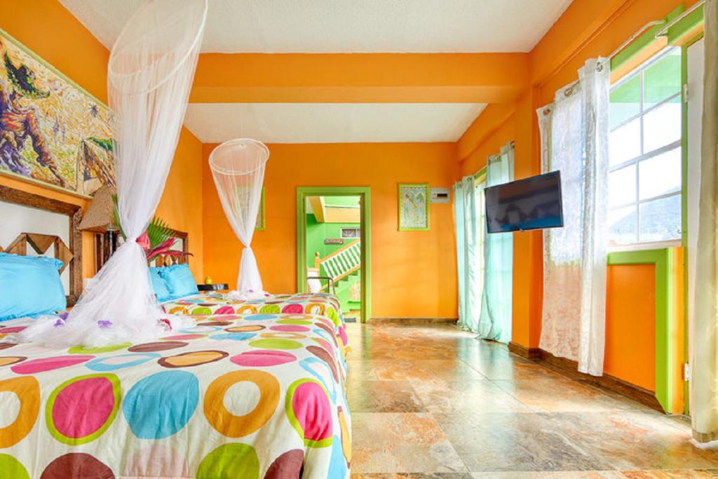 Schlafzimmer mit orangefarbenen Wänden und einem Bett mit einer farbenfrohen Tagesdecke in der Unterkunft Villa Des Pitons in Soufrière