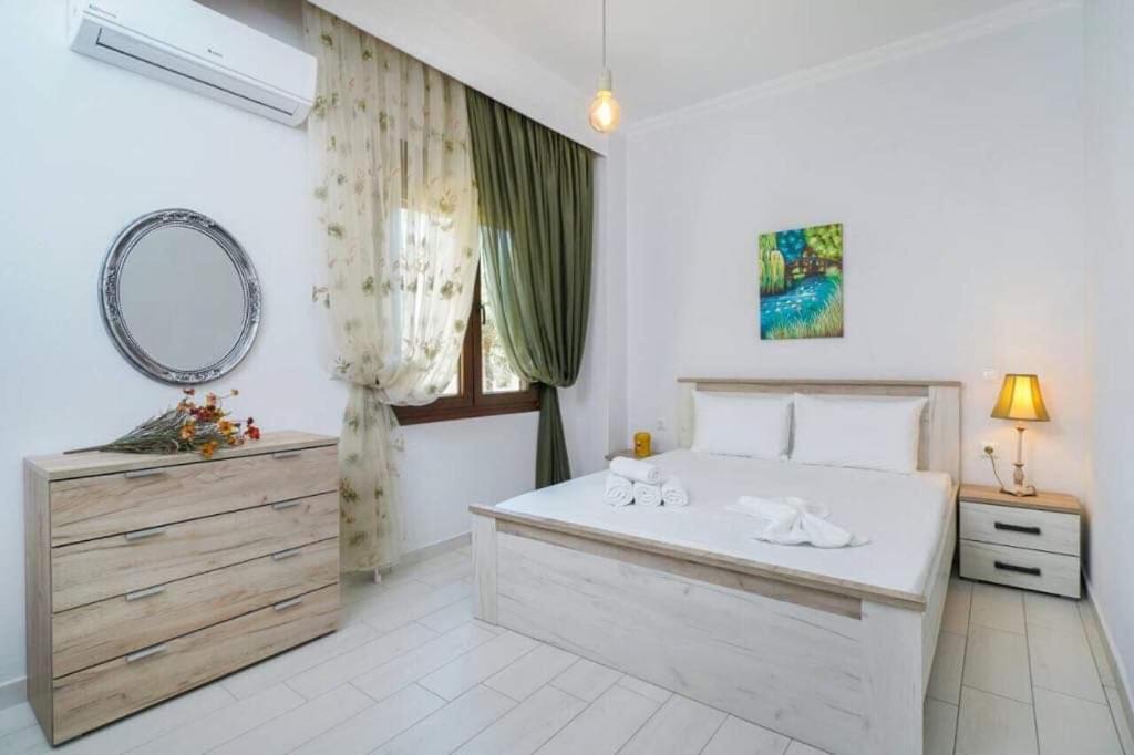 a white bedroom with a large bed and a mirror at Sevastiani’s Apartments in Skala Kallirachis