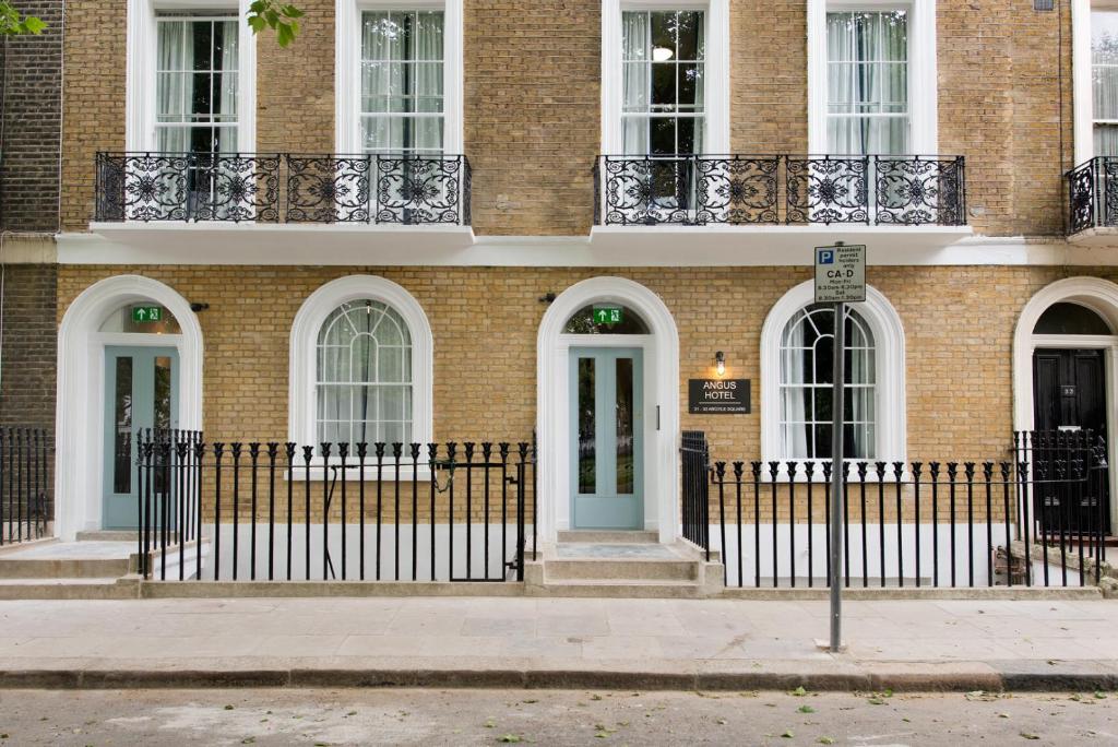 een bakstenen gebouw met witte ramen en een blauwe deur bij Angus Hotel in Londen