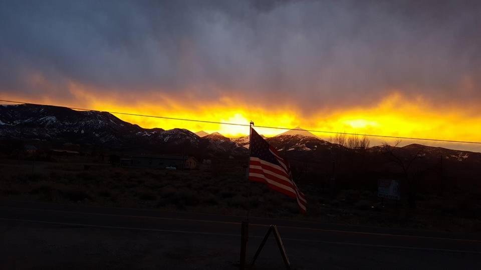 uma bandeira americana ao lado de uma estrada ao pôr-do-sol em The Whispering Elms Motel em Baker