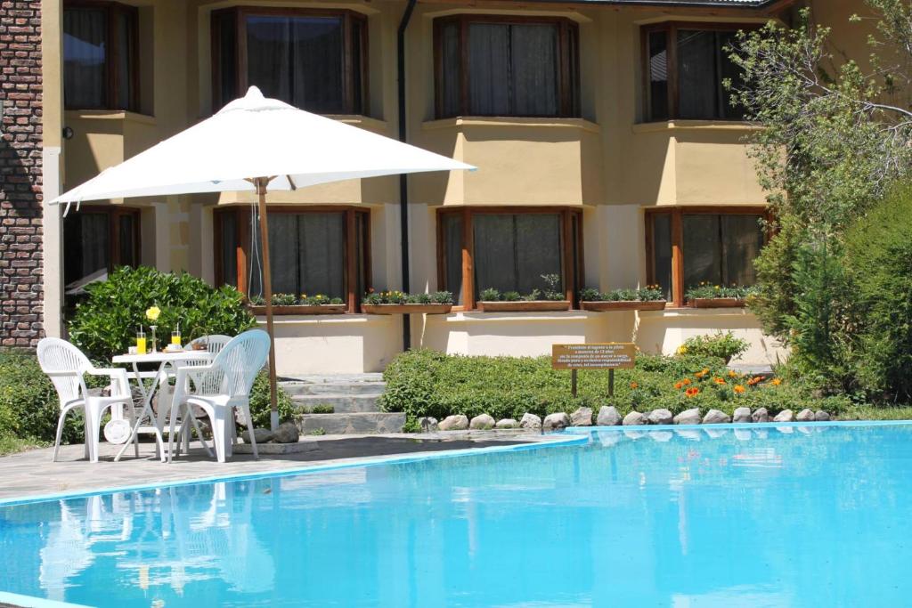 una mesa con sillas y una sombrilla junto a la piscina en Hosteria Las Lengas en San Martín de los Andes