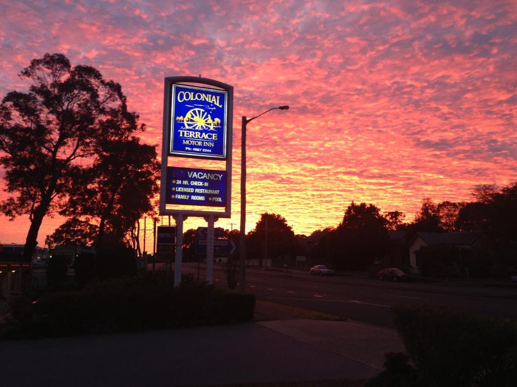 um sinal no lado de uma estrada com um pôr-do-sol em Colonial Terrace Motor Inn em Raymond Terrace