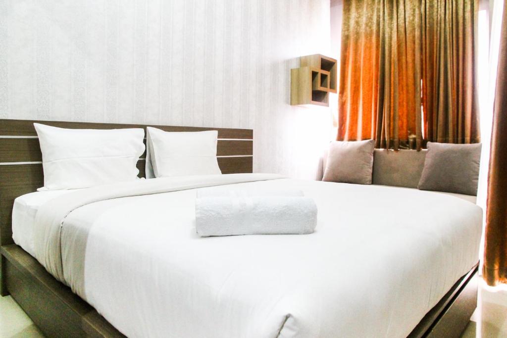 a bedroom with a large white bed with orange curtains at New Studio The Oasis Apartment By Travelio in Cikarang