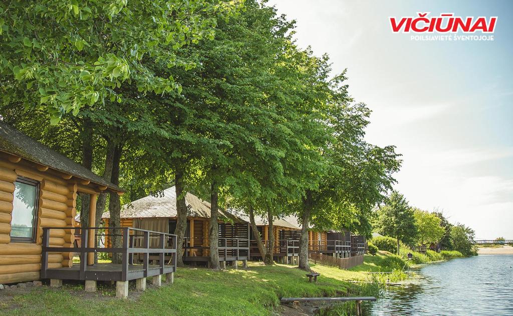 a row of wooden houses next to a river at Vičiūnų poilsiavietė Šventojoje in Šventoji