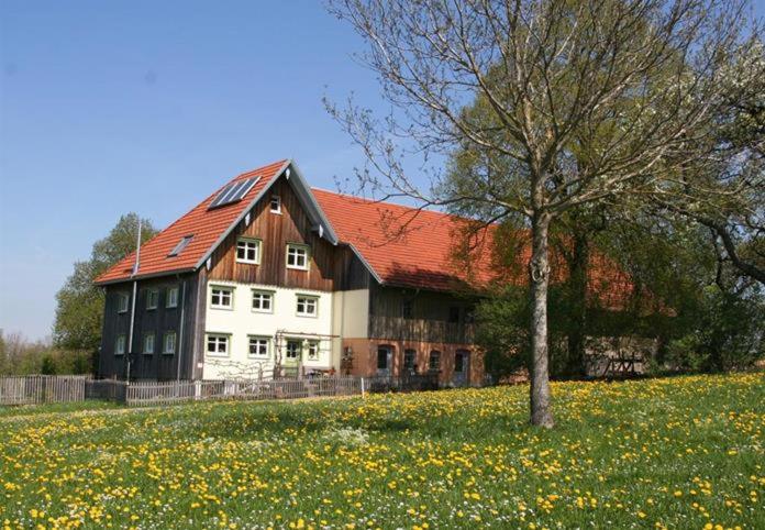 ein großes weißes Haus mit einem Baum auf einem Blumenfeld in der Unterkunft Schönhaar Schwenden 2 in Argenbühl