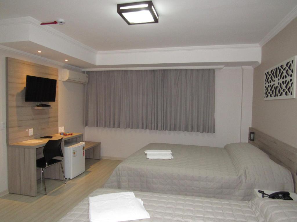 a hotel room with two beds and a desk at HOTEL MARIANI in Lajeado