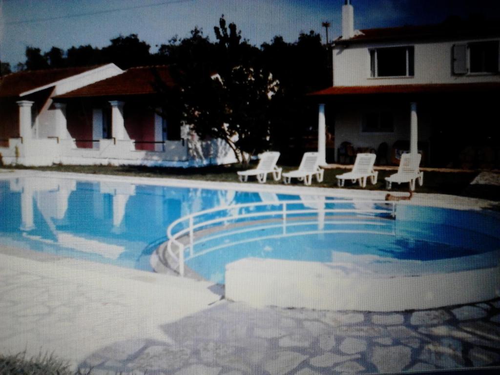 a swimming pool with white chairs and a house at Nikos Apartments in Acharavi
