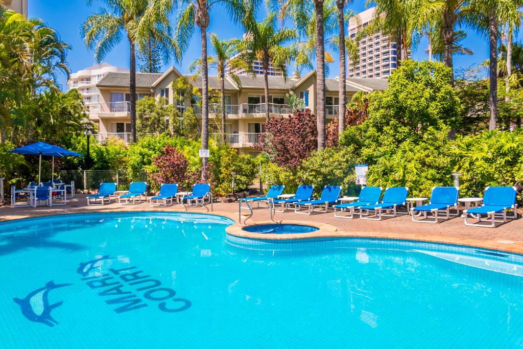 a swimming pool with blue chairs and palm trees at Mari Court Resort in Gold Coast