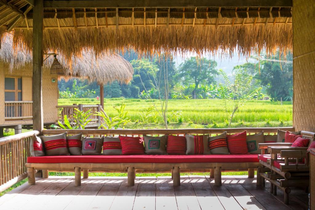 un banc avec des oreillers sur une terrasse couverte avec un champ dans l'établissement Lisu Lodge, à Mae Taeng