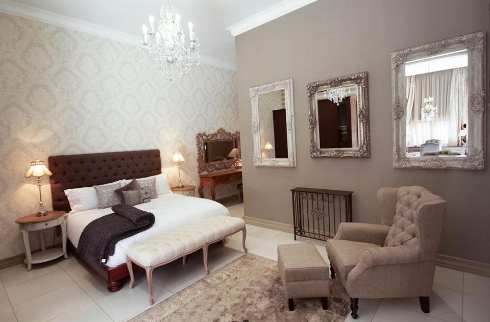 1 dormitorio con cama, silla y espejos en Tramonto Boutique Hotel, en Newcastle