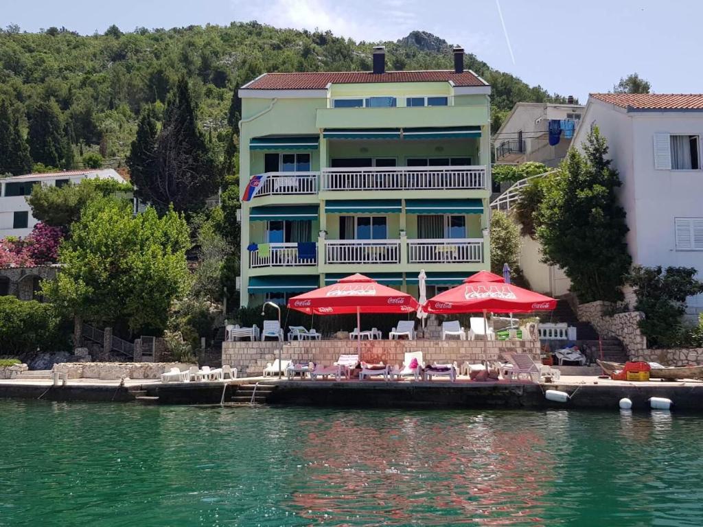 een gebouw met rode parasols en stoelen op het water bij Apartments Kocak in Blace