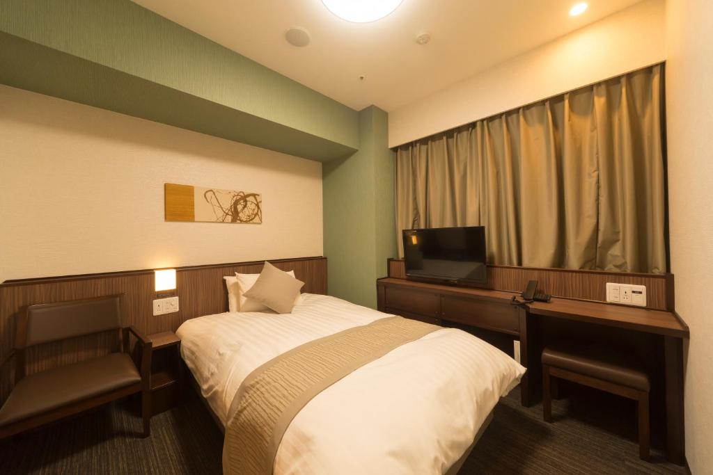 Habitación de hotel con cama, escritorio y TV. en Myoujin-no-Yu Dormy Inn Premium Kanda en Tokio