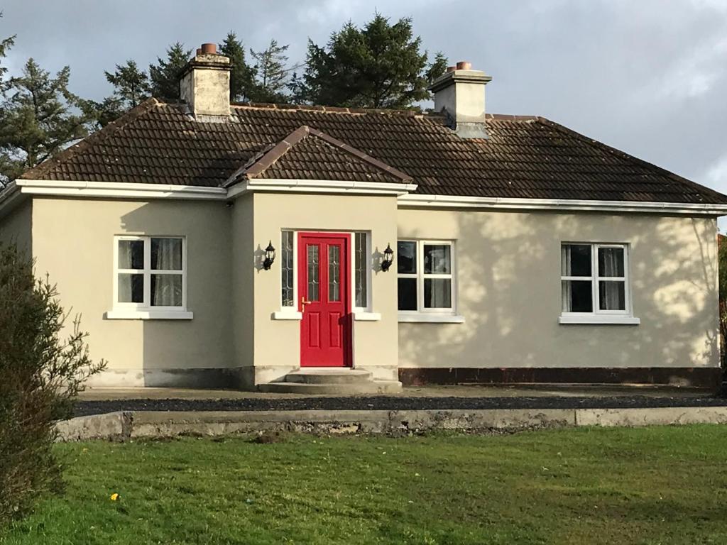 a small white house with a red door at Teach Fia in Ballina